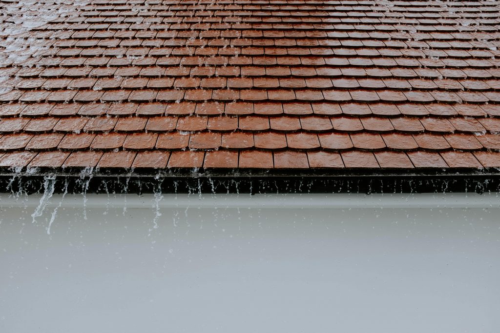 Brown roof tiles with rainwater cascading down, showcasing architectural texture and detail.