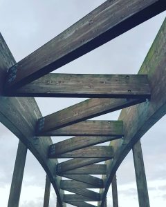 Dynamic view of a wooden bridge structure showcasing modern architectural design against a cloudy sky.